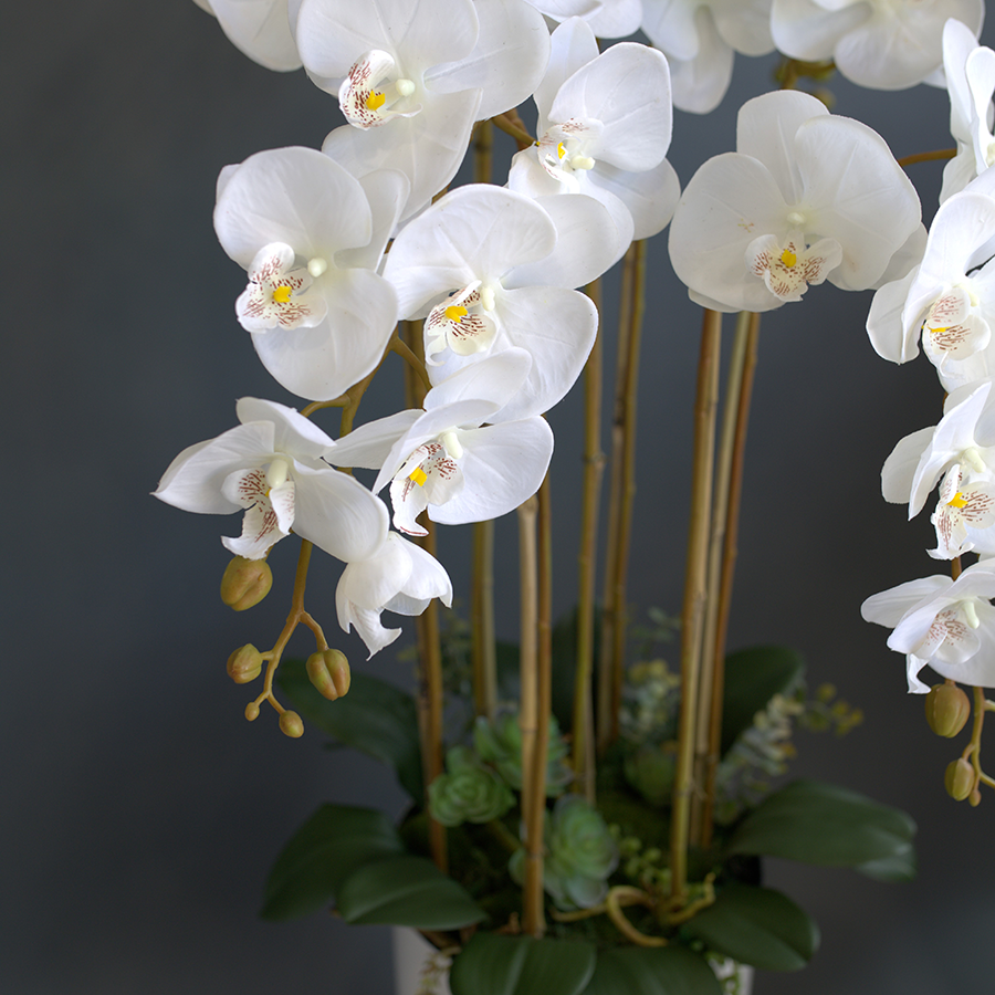 7 белых, искусственных фаленопсиса в высоком, напольном кашпо.